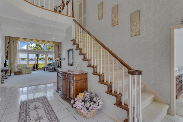 staircase with a water view, a towering ceiling, and tile patterned floors