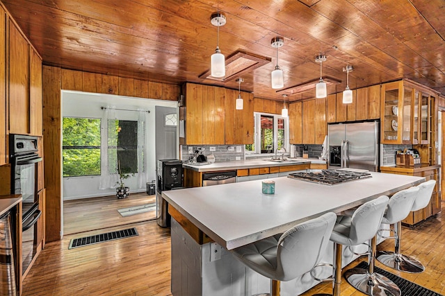 kitchen featuring appliances with stainless steel finishes, light wood-type flooring, hanging light fixtures, and wood ceiling