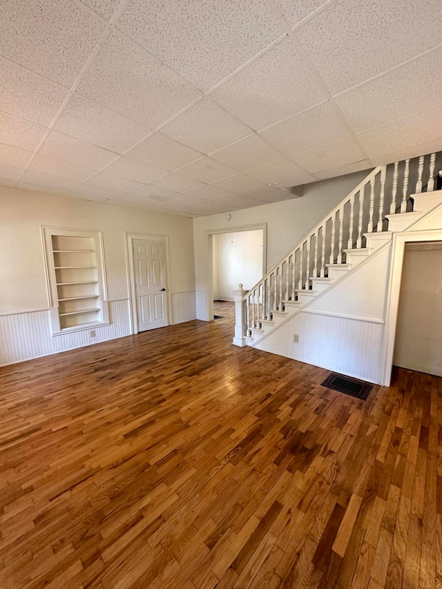 unfurnished living room with hardwood / wood-style floors, a paneled ceiling, and built in shelves