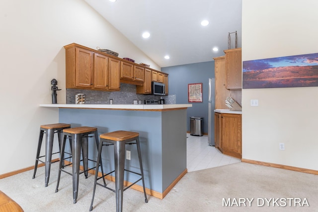 kitchen with tasteful backsplash, stainless steel microwave, brown cabinetry, a peninsula, and a kitchen breakfast bar