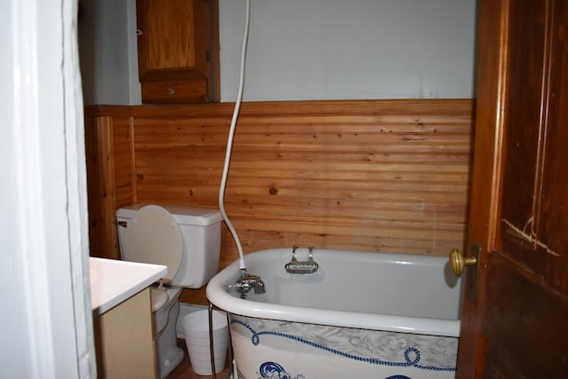 bathroom featuring a washtub, wood walls, toilet, and vanity