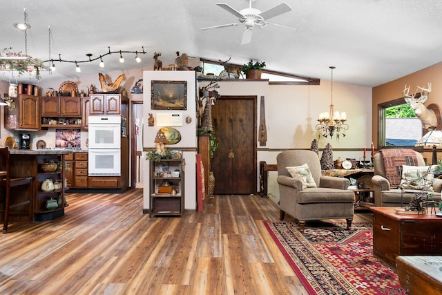 kitchen with white double oven, ceiling fan with notable chandelier, vaulted ceiling, decorative light fixtures, and dark hardwood / wood-style flooring