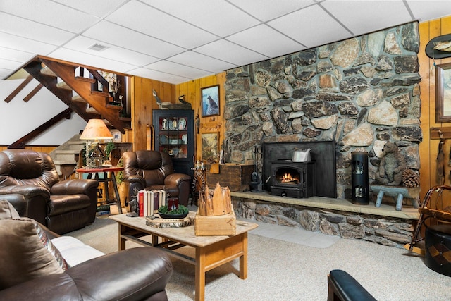 living room with a paneled ceiling, a wood stove, light carpet, and wooden walls