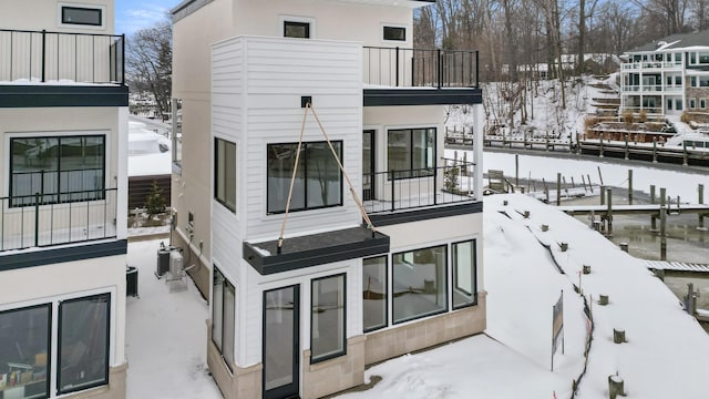 snow covered back of property with central AC unit and a balcony