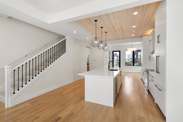 kitchen featuring sink, white cabinetry, a kitchen island with sink, pendant lighting, and light hardwood / wood-style floors