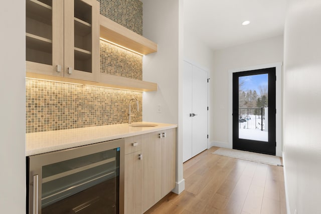 bar featuring wine cooler, sink, tasteful backsplash, light brown cabinets, and light wood-type flooring