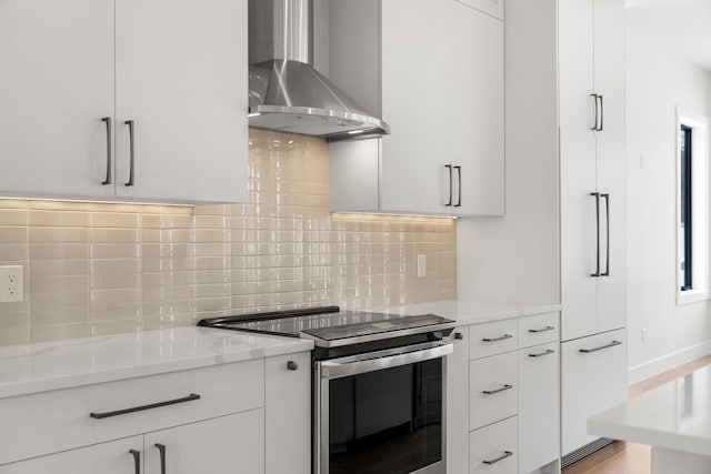 kitchen with light stone counters, white cabinetry, stainless steel range with electric cooktop, and wall chimney range hood