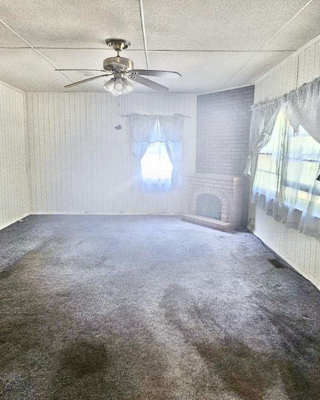 carpeted spare room featuring a fireplace, a drop ceiling, and ceiling fan