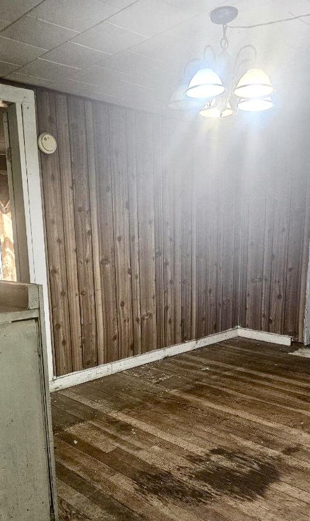 unfurnished room with wooden walls, an inviting chandelier, and dark wood-type flooring