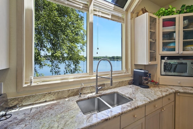 kitchen with a water view, light stone countertops, and sink