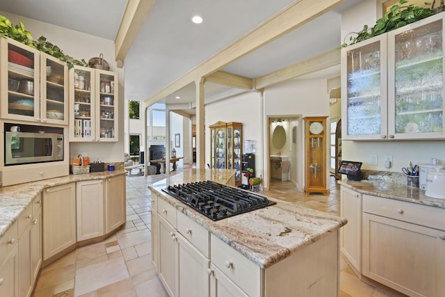 kitchen with light stone countertops, black gas stovetop, a kitchen island, and stainless steel microwave