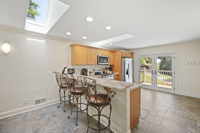 kitchen featuring a skylight, a kitchen breakfast bar, kitchen peninsula, stainless steel appliances, and french doors