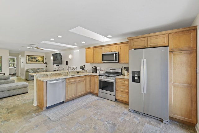 kitchen featuring sink, light stone counters, a skylight, kitchen peninsula, and stainless steel appliances