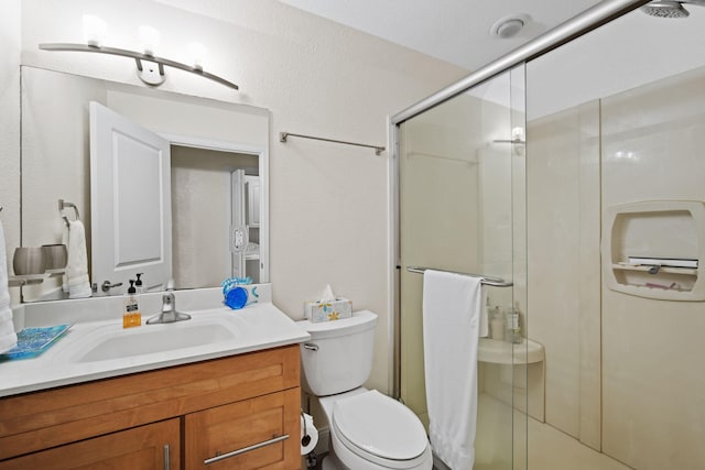 bathroom featuring a shower with door, vanity, and toilet