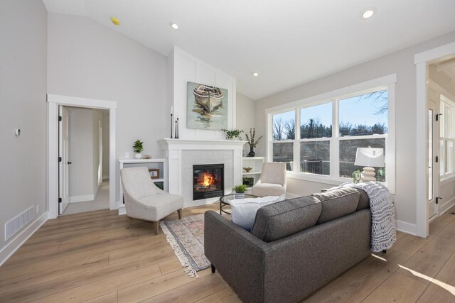 living room with high vaulted ceiling, a fireplace, and light hardwood / wood-style floors