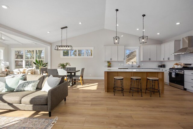 kitchen with wall chimney exhaust hood, gas range, decorative light fixtures, a center island, and white cabinets