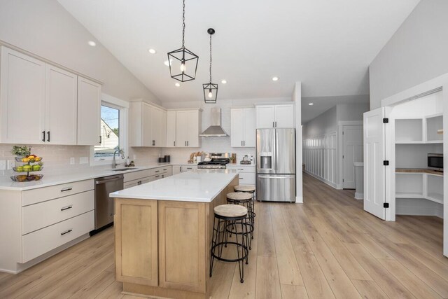 kitchen with sink, appliances with stainless steel finishes, a kitchen island, wall chimney range hood, and white cabinets