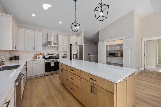 kitchen with wall chimney range hood, white cabinetry, hanging light fixtures, stainless steel appliances, and a center island