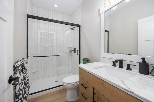 bathroom with hardwood / wood-style flooring, vanity, toilet, and a shower with shower door