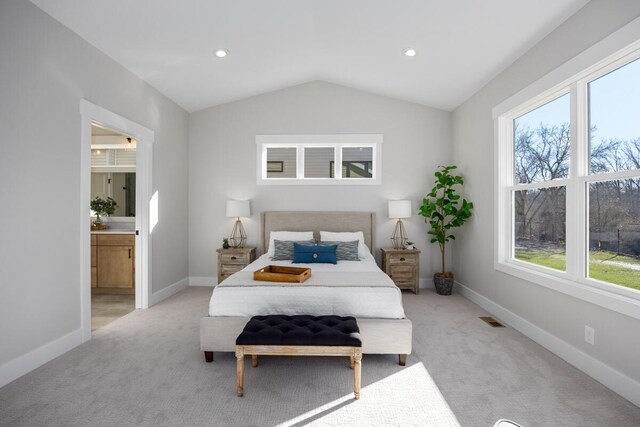 carpeted bedroom with lofted ceiling, multiple windows, and ensuite bathroom