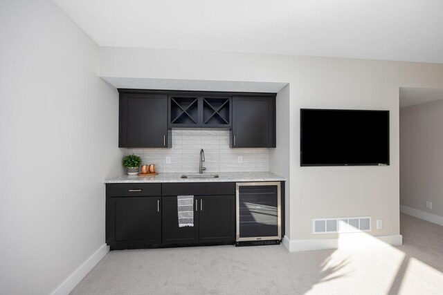 bar with sink, tasteful backsplash, light stone countertops, light colored carpet, and beverage cooler