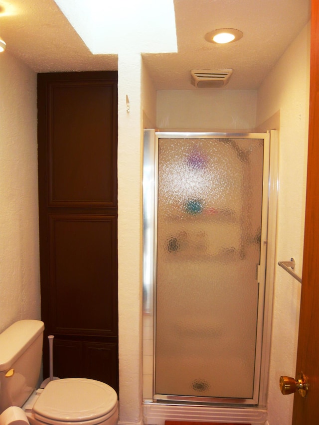 bathroom featuring a shower with door and toilet