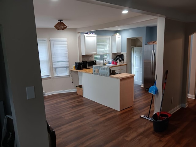 kitchen with dark wood-type flooring, wooden counters, appliances with stainless steel finishes, kitchen peninsula, and white cabinets