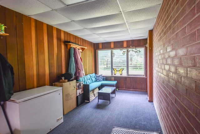 living area with wooden walls, carpet, and a drop ceiling