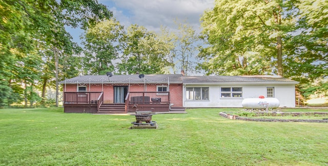 rear view of property featuring brick siding, an outdoor fire pit, a lawn, a chimney, and a deck