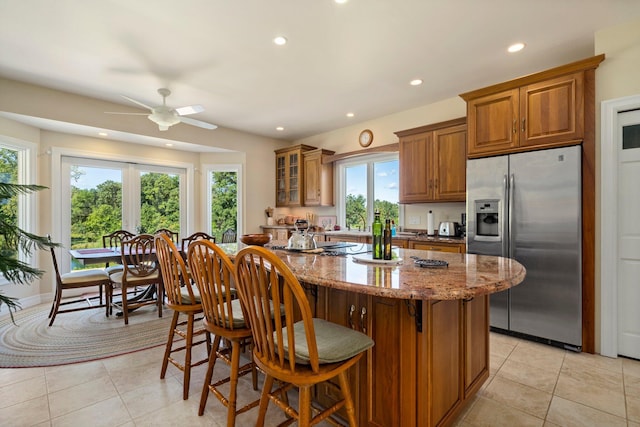 kitchen featuring light tile patterned floors, stainless steel fridge, light stone countertops, and a kitchen breakfast bar