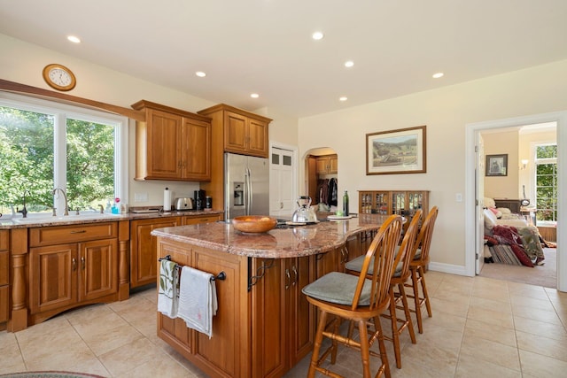 kitchen with a kitchen island, a breakfast bar, sink, light stone counters, and stainless steel refrigerator with ice dispenser