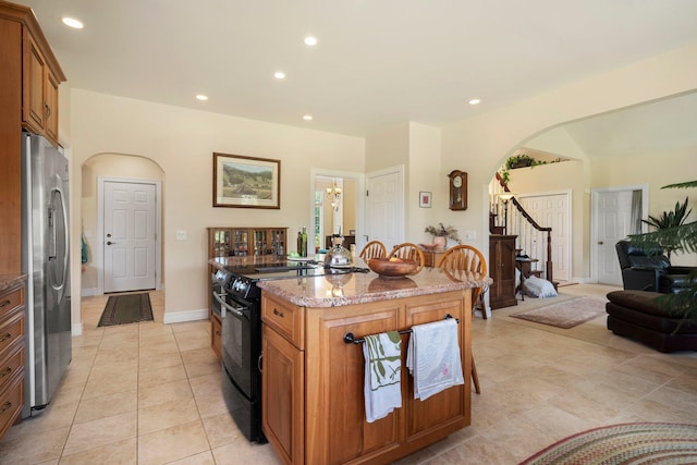 kitchen with stainless steel refrigerator, black range with electric stovetop, a kitchen breakfast bar, a center island, and light stone countertops