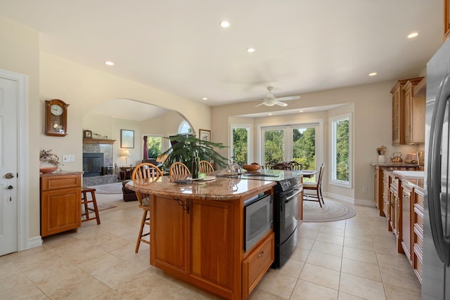 kitchen featuring light tile patterned floors, a breakfast bar, stone counters, stainless steel appliances, and a center island