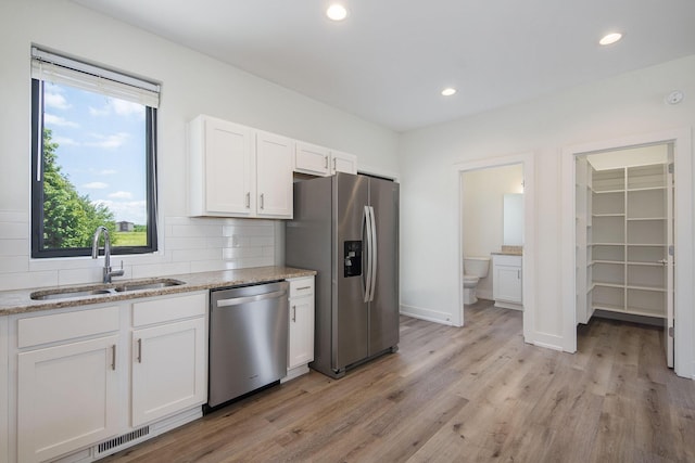 kitchen with sink, stainless steel appliances, light stone counters, backsplash, and white cabinets