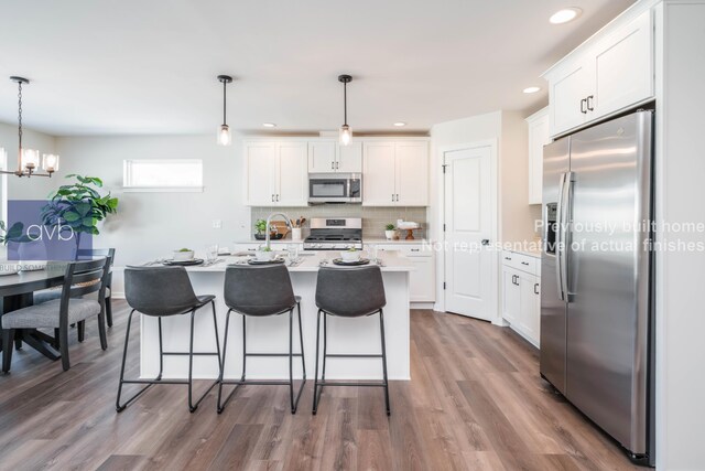 kitchen featuring white cabinetry, hanging light fixtures, a kitchen island with sink, and appliances with stainless steel finishes