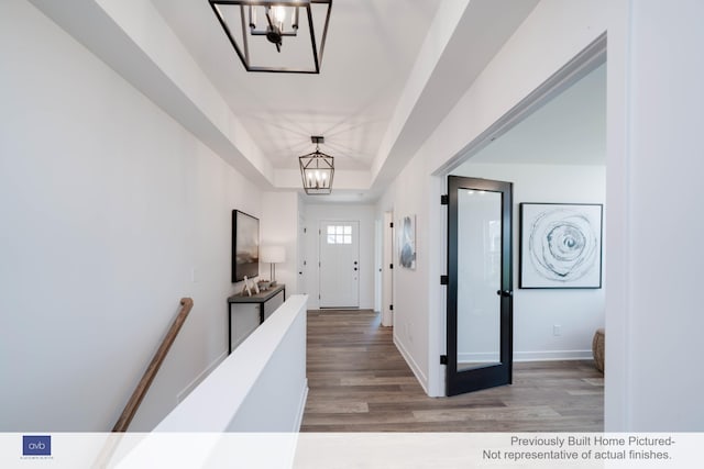 hall with light hardwood / wood-style flooring, an inviting chandelier, and a tray ceiling