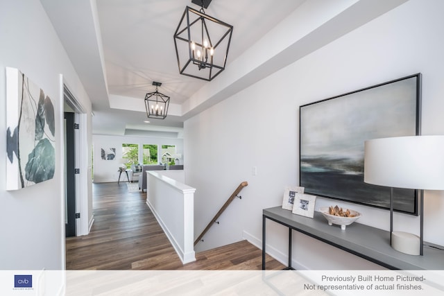 hallway featuring dark hardwood / wood-style flooring, a raised ceiling, and a chandelier