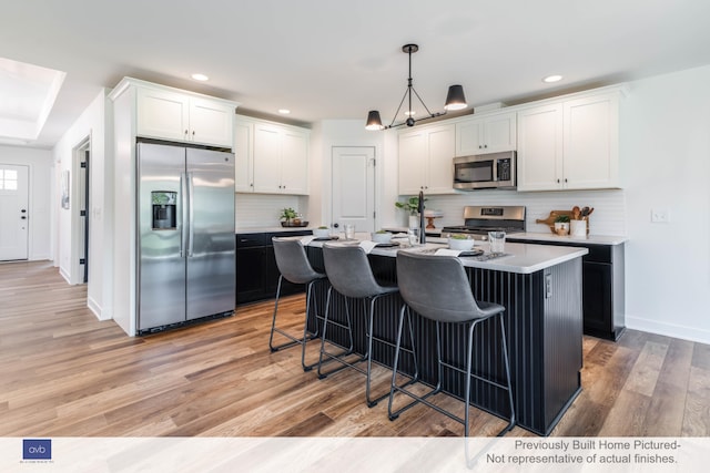 kitchen with a kitchen island with sink, light hardwood / wood-style floors, white cabinets, and appliances with stainless steel finishes