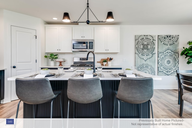 kitchen featuring tasteful backsplash, white cabinetry, appliances with stainless steel finishes, and an island with sink