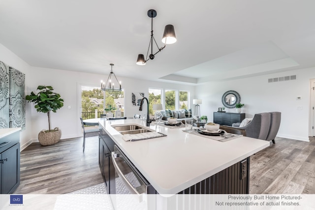 kitchen with dishwasher, sink, hanging light fixtures, a raised ceiling, and a center island with sink