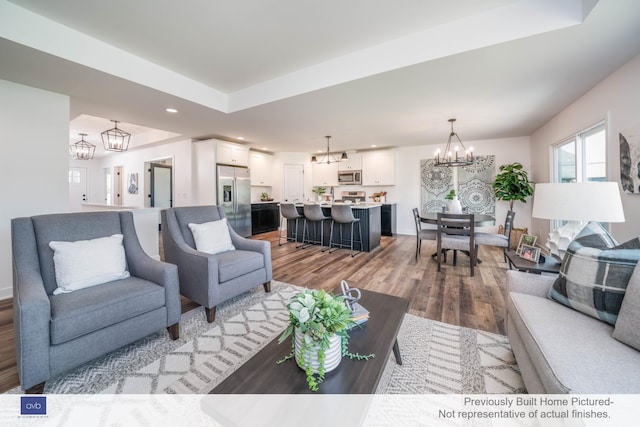 living room with a notable chandelier, hardwood / wood-style flooring, and a raised ceiling