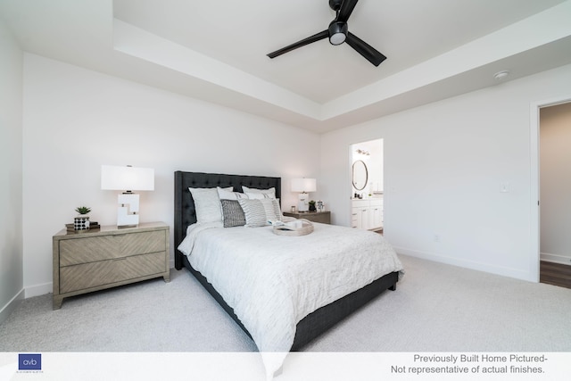 bedroom with ceiling fan, a tray ceiling, light colored carpet, and ensuite bath