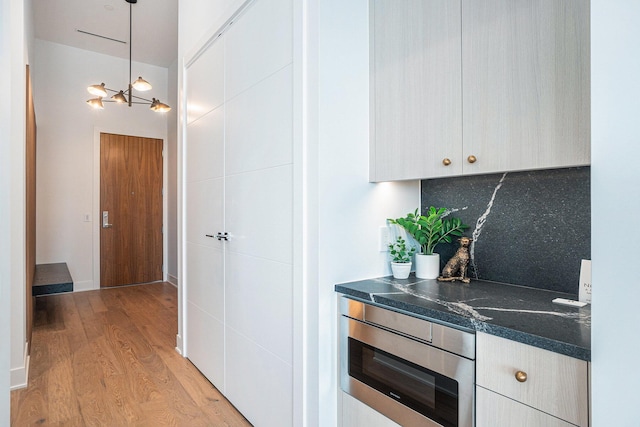 interior space featuring an inviting chandelier, stainless steel microwave, light hardwood / wood-style floors, decorative backsplash, and decorative light fixtures