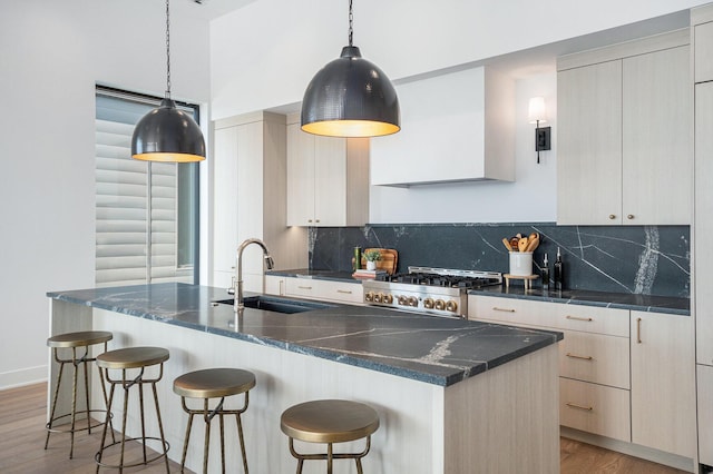 kitchen featuring sink, tasteful backsplash, hanging light fixtures, an island with sink, and stove