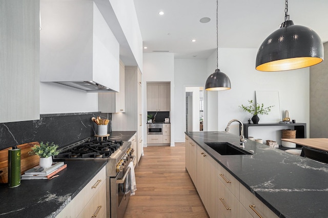 kitchen featuring sink, stainless steel range, decorative light fixtures, and dark stone counters