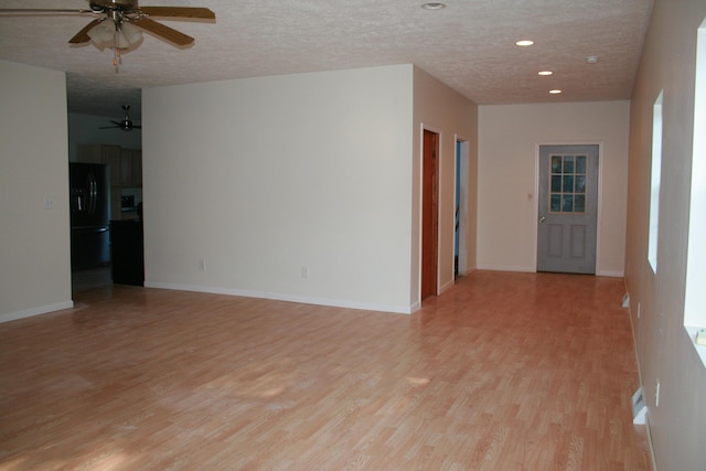 empty room with ceiling fan, light hardwood / wood-style flooring, and a textured ceiling