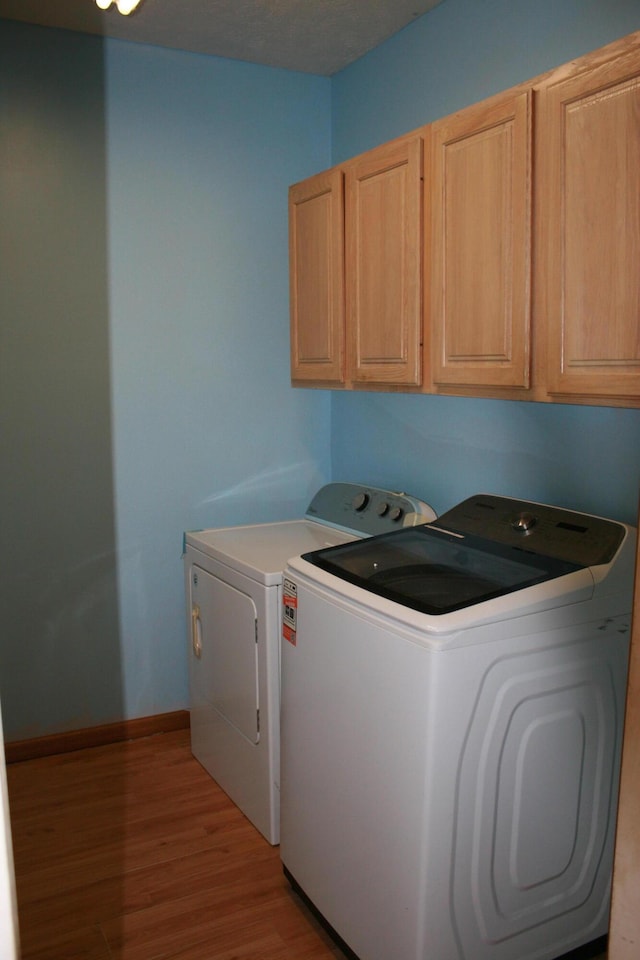 laundry area with cabinets, washer and clothes dryer, and light wood-type flooring