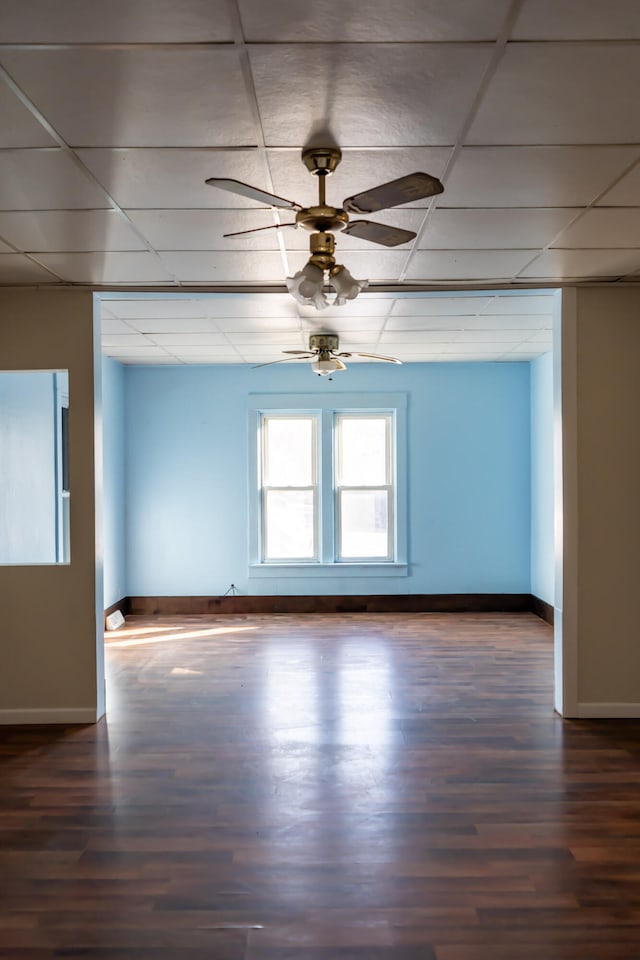 empty room with dark wood-type flooring, a paneled ceiling, and ceiling fan