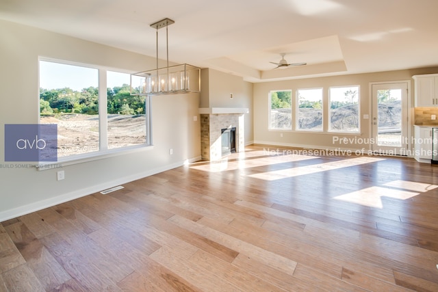 unfurnished living room with a raised ceiling, ceiling fan with notable chandelier, a fireplace, and light hardwood / wood-style flooring