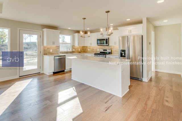 kitchen featuring light hardwood / wood-style flooring, hanging light fixtures, appliances with stainless steel finishes, a kitchen island, and white cabinets